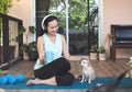 Woman wearing headphones, holding coffee cup, sitting  on yoga mat in balcony  with computer laptop Chihuahua dog, smiling and rub Royalty Free Stock Photo