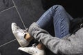 A woman wearing jean and white sneakers touching her leg while sitting on the floor