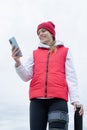 Woman wearing knee brace or orthosis after leg surgery walking in the park using smartphone