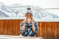 Woman wearing knitting hat and holding hot drink mug outdoor on a wooden terrace in winter mountains Royalty Free Stock Photo