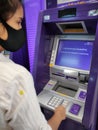 Woman wearing a mask and withdrawing money at the ATM.