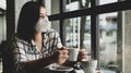 A woman wearing a medical mask sits in a coffee shop looking out the window with sad eyes Royalty Free Stock Photo