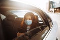 Woman wearing a medical sterile mask in taxi car on a backseat looking out of window checking her cell phone. Girl passenger Royalty Free Stock Photo