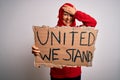 Woman wearing muslim hijab asking for union holding banner with united stand message stressed with hand on head, shocked with Royalty Free Stock Photo