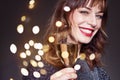 Woman wearing night party dress with a glass of champagne on dark background. Lady with long curly hair and perfect teeth celebrat