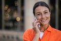 Woman wearing orange shirt standing in city street talking via mobile phone. Royalty Free Stock Photo