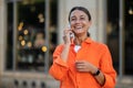 Woman wearing orange shirt standing in city street talking via mobile phone. Royalty Free Stock Photo