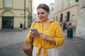 Woman wearing orange yellow shirt texting on the smart phone walking in the street in a sunny day Royalty Free Stock Photo