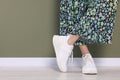 Woman wearing pair of new stylish sneakers near dark olive wall, closeup. Space for text