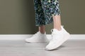 Woman wearing pair of new stylish sneakers near dark olive wall, closeup