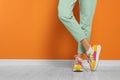 Woman wearing pair of new stylish sneakers near orange wall, closeup. Space for text