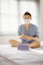 Woman wearing protection mask sitting on bed in home living room watching on computer tablet : work from home concept