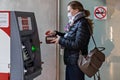 A woman wearing a protective medical mask on her face inserting a credit bank card and withdrawing cash from an ATM