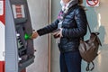 A woman wearing a protective medical mask on her face inserting a credit bank card and withdrawing cash from an ATM