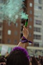 Woman wearing a purple feminist scarf holds in her hand a flare that releases green smoke