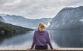 Woman wearing purple hoodie watching tranquil overcast morning scene at lake Bohinj, Alps mountains, Slovenia.