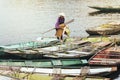 Woman wearing purple shirt, conical hat carry paddles and mat, walking on boat with many boats stop over the river at Trang An Gro