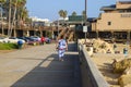 A woman wearing a purple tie-dye shirt walking along a bike path at the beach surrounded by tall lush green palm trees