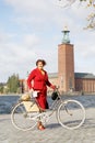 Woman wearing red dress holding a vintage bicycle in front of Stockholm City Hall Royalty Free Stock Photo