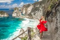 Woman wearing a red dress on standing on the stairs leading down at Diamond beach in Nusa Penida, Bali, Indonesia. Royalty Free Stock Photo