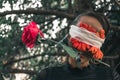 Woman with red flowers bandaged to her eyes with a rose in her mouth