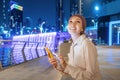 Woman wearing red turban is typing or using app on her smartphone against the neon-lit backdrop of a waterfall from a bridge