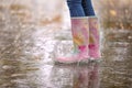 Woman wearing rubber boots splashing in puddle after rain, focus on legs