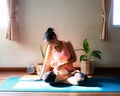 Woman wearing sportwear sitting on yoga mat in morning sunlight playing with her Chihuchua dog on her lap Royalty Free Stock Photo