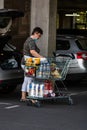 Woman wearing surgical mask with shopping cart full of goods, putting groceries in car trunk. Bucharest, Romania, 2020 Royalty Free Stock Photo