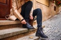 Woman wearing trench coat sitting on stairs and tying shoelace on her black boot Royalty Free Stock Photo