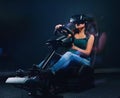 Woman wearing VR headset driving on car racing simulator cockpit with seat and wheel. Royalty Free Stock Photo