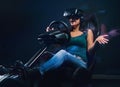 Young woman wearing VR headset having fun while driving on car racing simulator cockpit with seat and wheel.