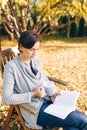 Woman wearing warm knit clothes drinking a cup of hot tea or coffee and reading a book outdoors in sunlight - season, literature Royalty Free Stock Photo