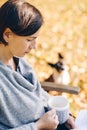 Woman wearing warm knit clothes drinking a cup of hot tea or coffee and reading a book outdoors in sunlight - season, literature Royalty Free Stock Photo