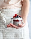 A woman wearing a white apron holding a mason jar with chai pudding topped with fresh berry fruit