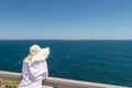 Woman wearing white shirt with white hat looking into the ocean at Cape Spencer