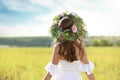 Young woman wearing wreath made of beautiful flowers in field on sunny day, back view Royalty Free Stock Photo