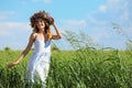 Young woman wearing wreath made of beautiful flowers in field on sunny day Royalty Free Stock Photo