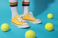 Woman wearing yellow classic old school sneakers and tennis balls on light blue background, closeup Royalty Free Stock Photo