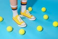 Woman wearing yellow classic old school sneakers and tennis balls on light blue background, closeup Royalty Free Stock Photo