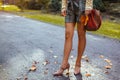 Woman wears stylish brown high-heeled shoesholding handbag in autumn park standing among falling leaves Royalty Free Stock Photo