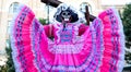 Woman wears sugar skull mask and bright pink Jalisco dress in celebration of Dia de los Muertos / Day of the Dead