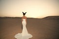 Woman in wedding dress in desert. Sensual woman with brunette hair. Bride in white gown on sunset sky, back view Royalty Free Stock Photo