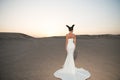 Woman in wedding dress in desert. Sensual woman with brunette hair. Bride in white gown on sunset sky, back view. Fashion model in Royalty Free Stock Photo