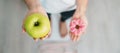 woman on weight scale and hand hold green Apple and donut, choose between fruit is Healthy and sweet is Unhealthy junk food. Royalty Free Stock Photo