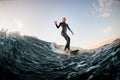 woman in wetsuit wakesurfing on the board and riding down the river wave and show hand gesture