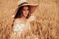 Woman wheat field nature. Happy young woman in sun hat in summer wheat field at sunset. Copy space, sunset, flare light