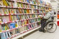 A woman in a wheelchair chooses a book for a child in the children`s department of the store. Royalty Free Stock Photo