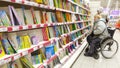 A woman in a wheelchair chooses a book for a child in the children`s department of the store. Royalty Free Stock Photo