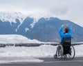 A woman in a wheelchair holds her hands in the shape of a heart in the mountains in winter.